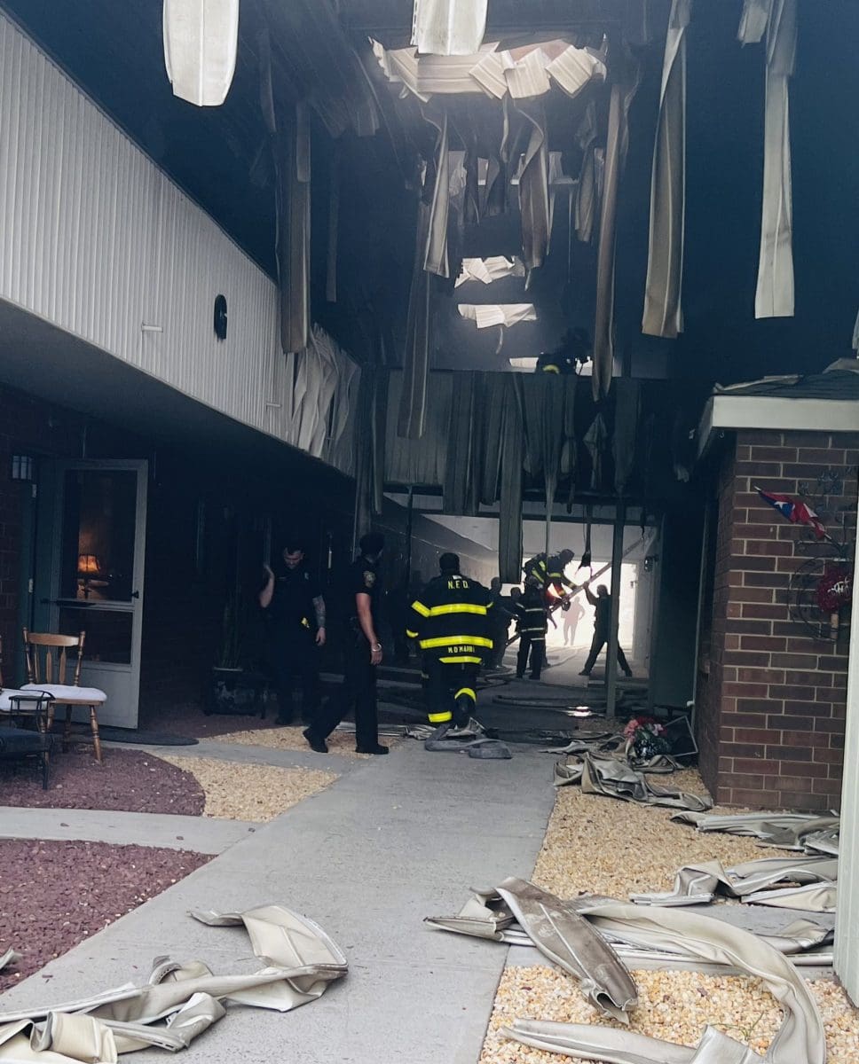 Norwalk firefighters and police between two buildings, with evidence of fire damage over their heads.
