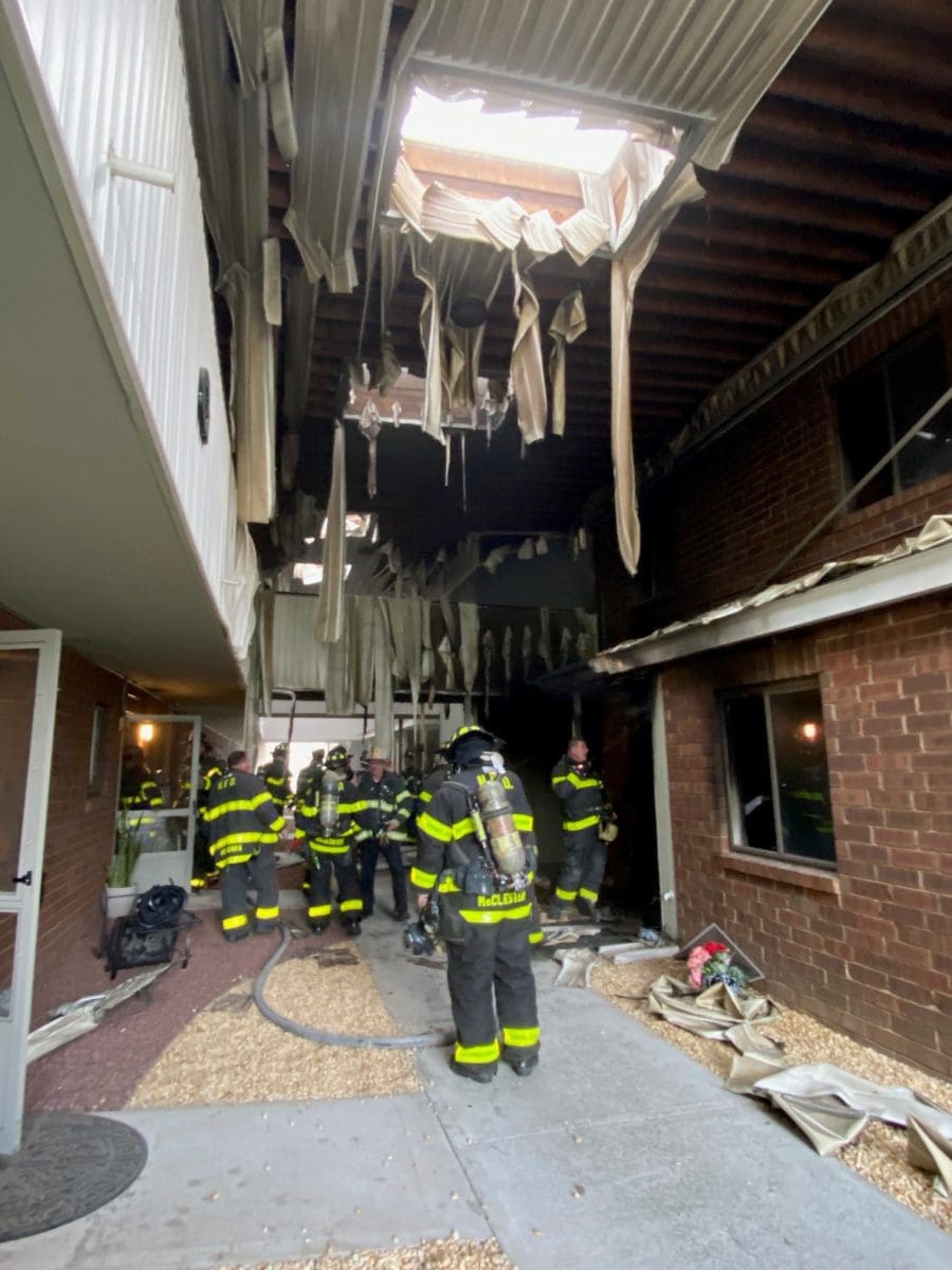 Norwalk firefighters between two buildings, with evidence of fire damage over their heads.