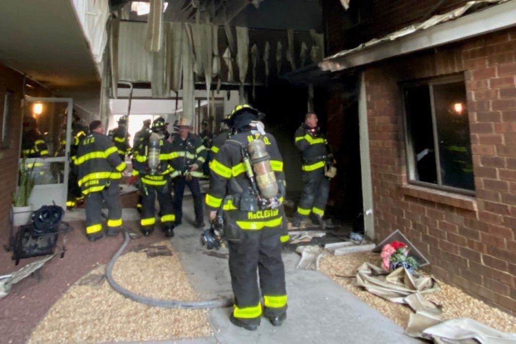 Norwalk firefighters between two buildings, with evidence of fire damage over their heads.